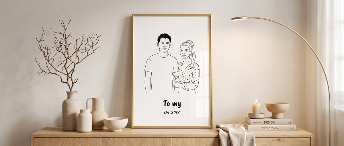 Portret line art z podpisem w złotej ramie na jasnej konsoli z ceramiką, gałązką w wazonie i lampą łukową